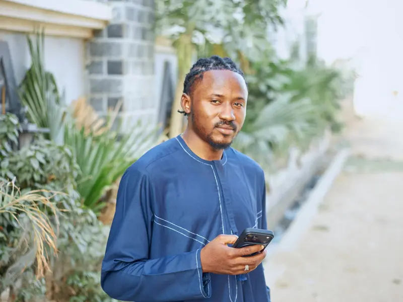 Un homme consulte son téléphone devant un logement.